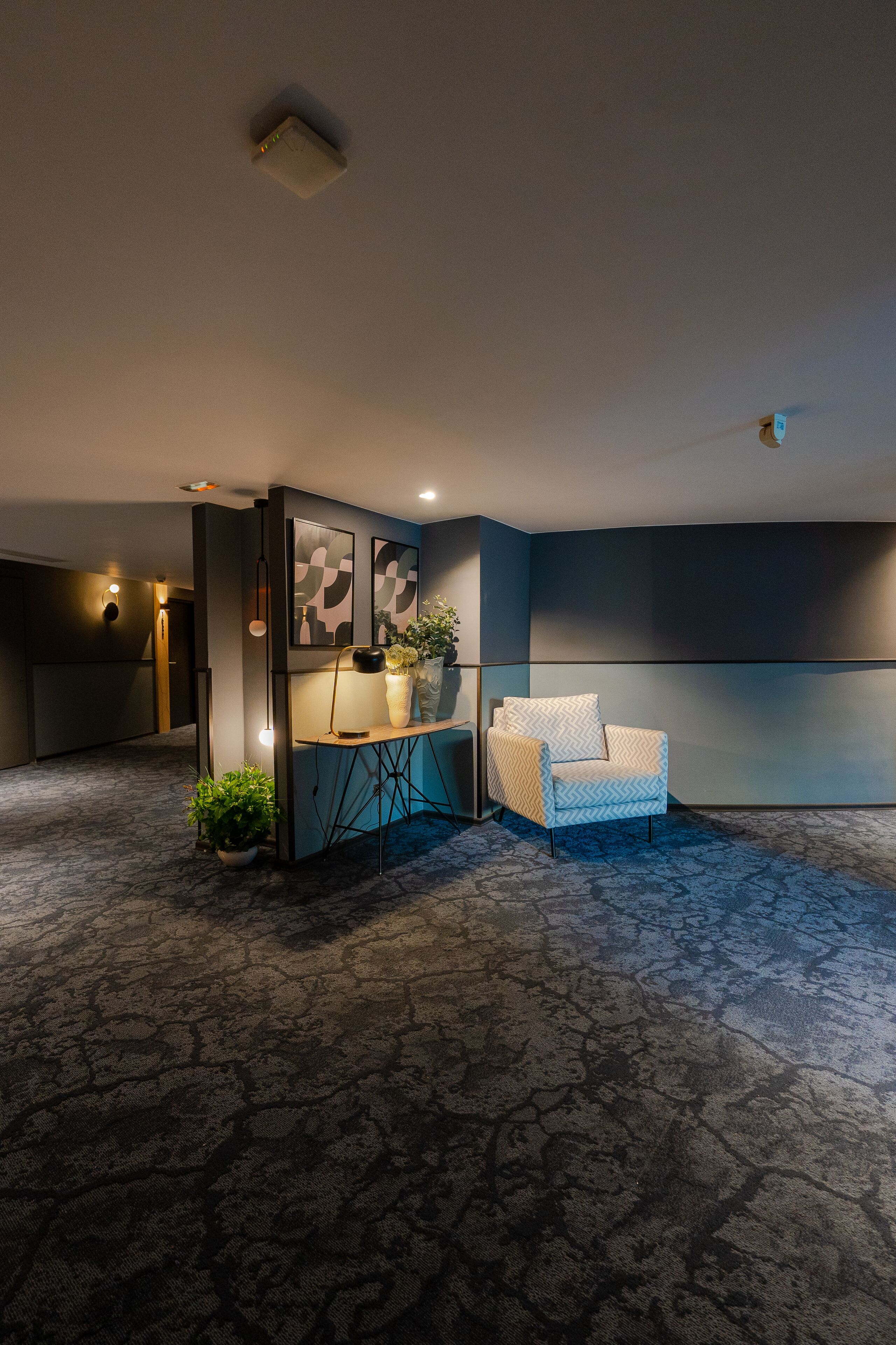 A modern hotel lobby with a seating area, a reception desk, and a large wall with a screen.