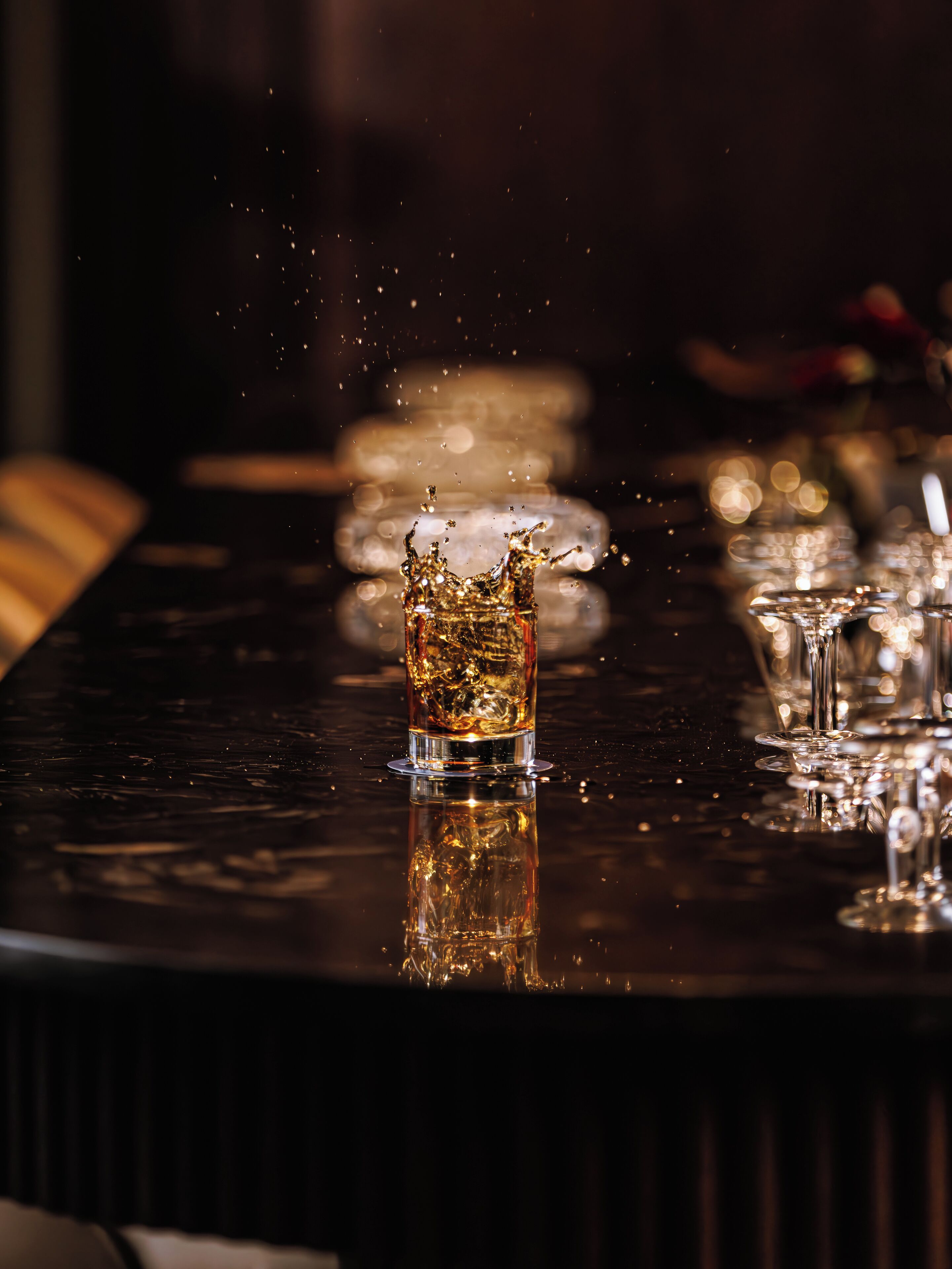 A bar setting with a glass of whiskey and ice cubes, glasses, and a bar counter.
