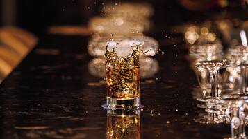 A bar setting with a glass of whiskey and ice cubes, glasses, and a bar counter.