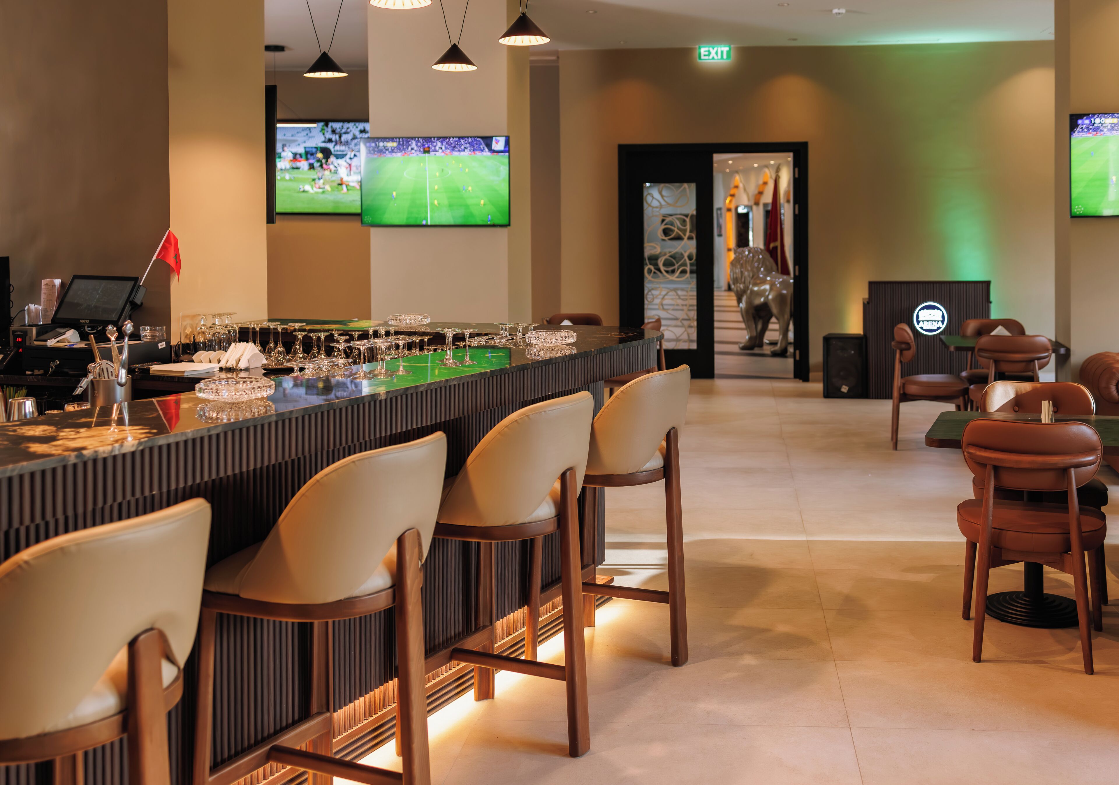 Zona de bar con varias sillas, una barra con vasos y botellas, y un televisor mostrando un partido deportivo.