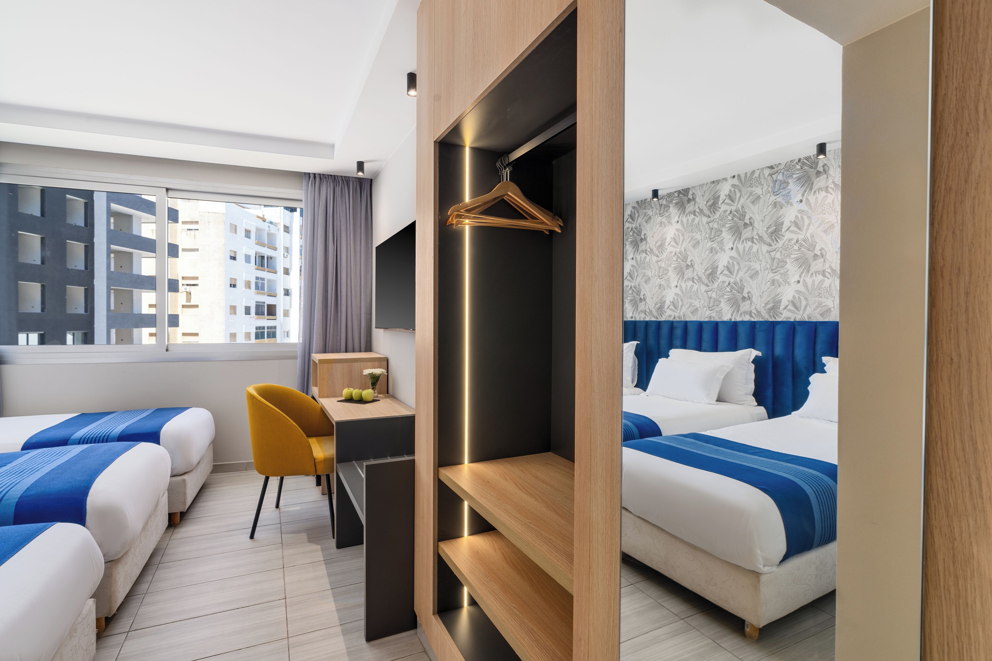 A hotel room with two beds, a desk, a chair, and a wardrobe.