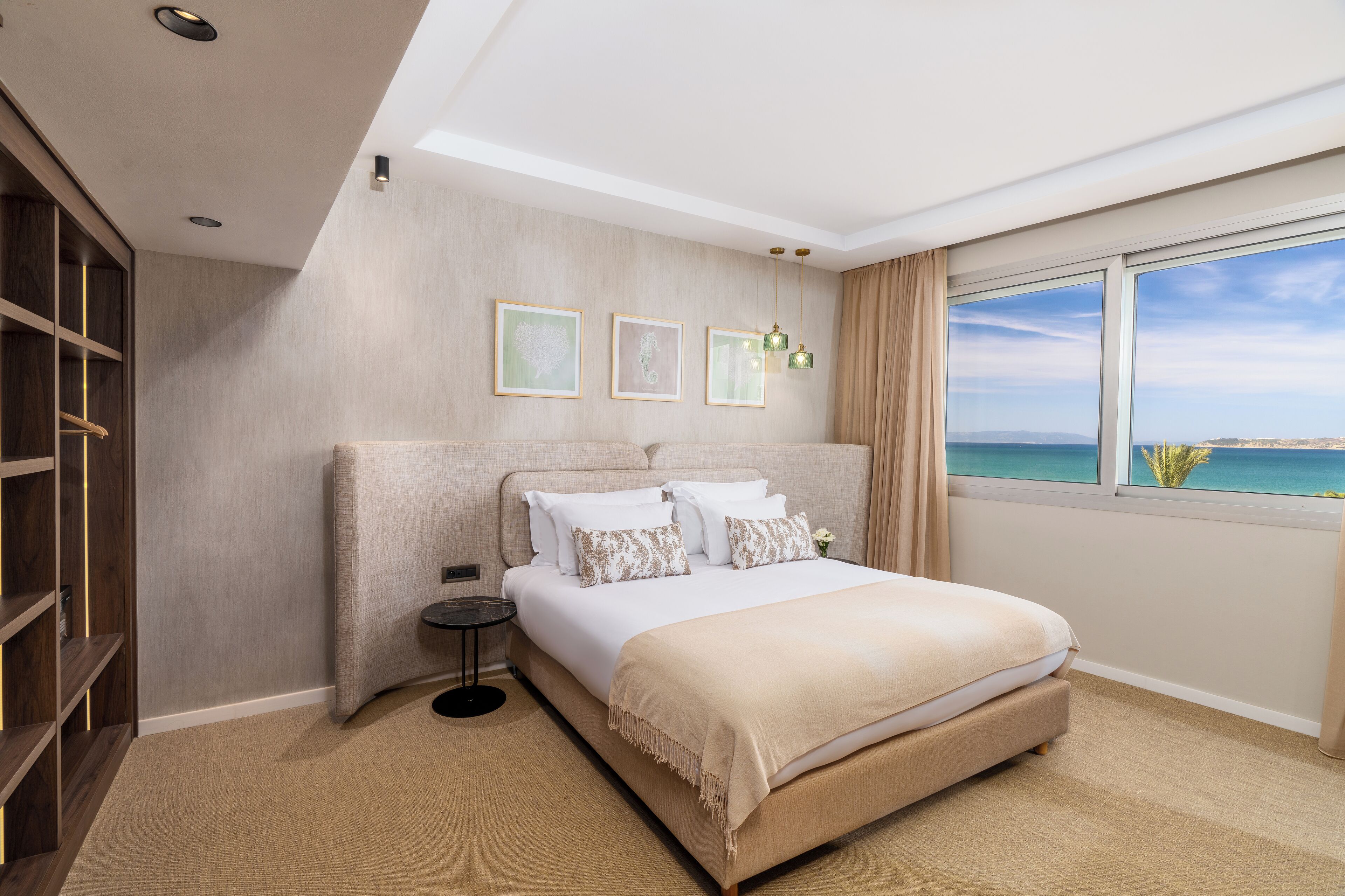 A modern bedroom with a large bed, a built-in wardrobe, and a view of the sea.