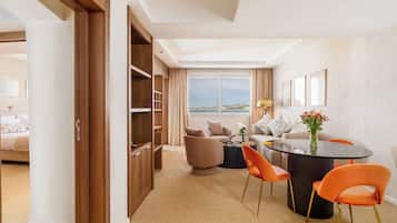 Una habitación de hotel moderna con un ventanal grande, una zona de comedor con sillas color naranja, una mesa redonda y un sofá.