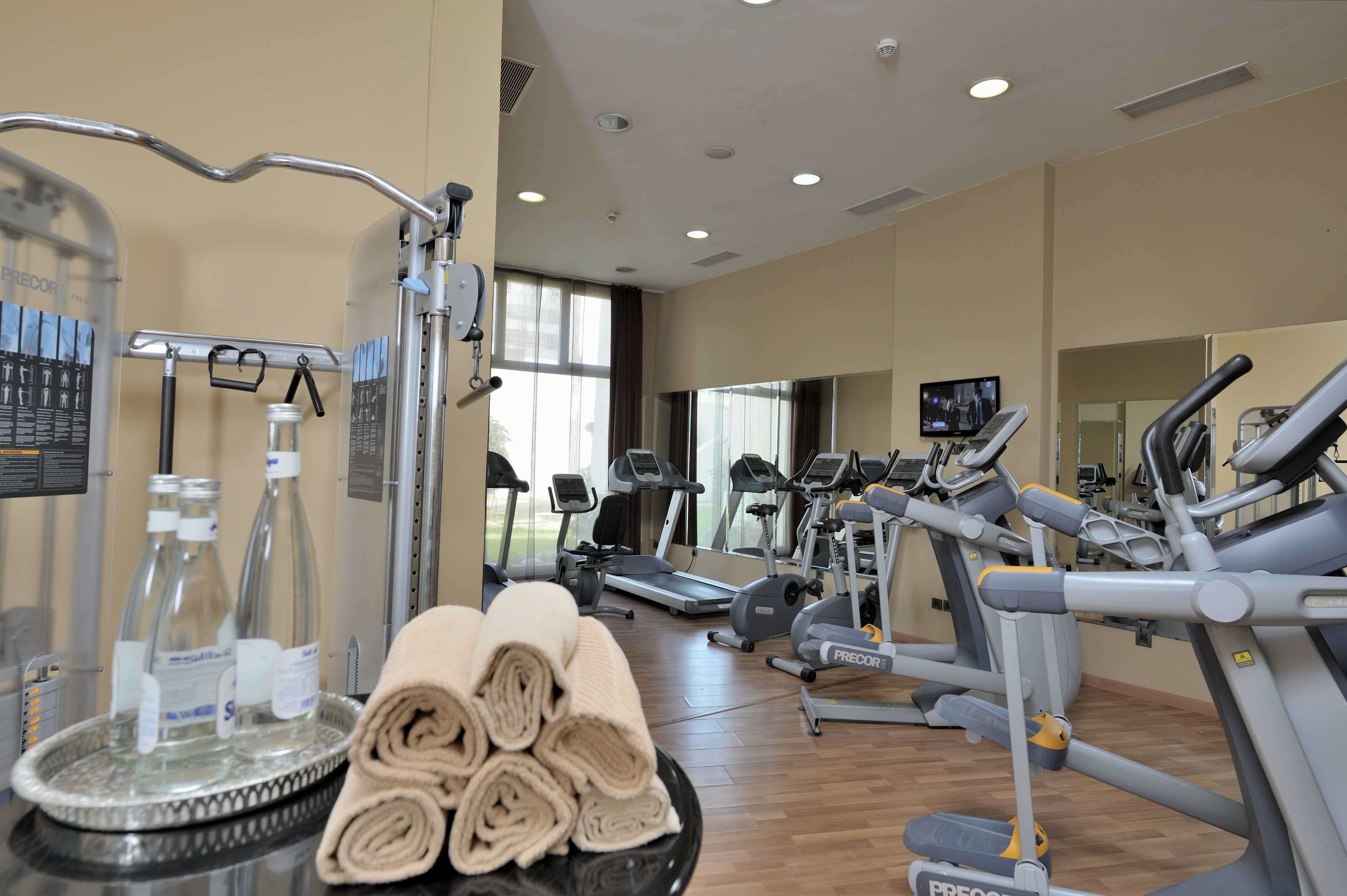 A gym with various exercise equipment, including treadmills and ellipticals, and a water station with bottles and towels.
