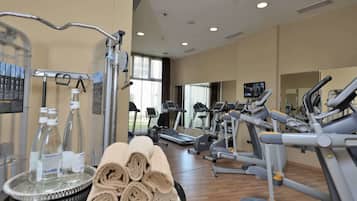 Une salle de sport équipée de divers appareils d’exercice, notamment des tapis de course et des vélos elliptiques, ainsi qu’un point d’eau avec des bouteilles et des serviettes.