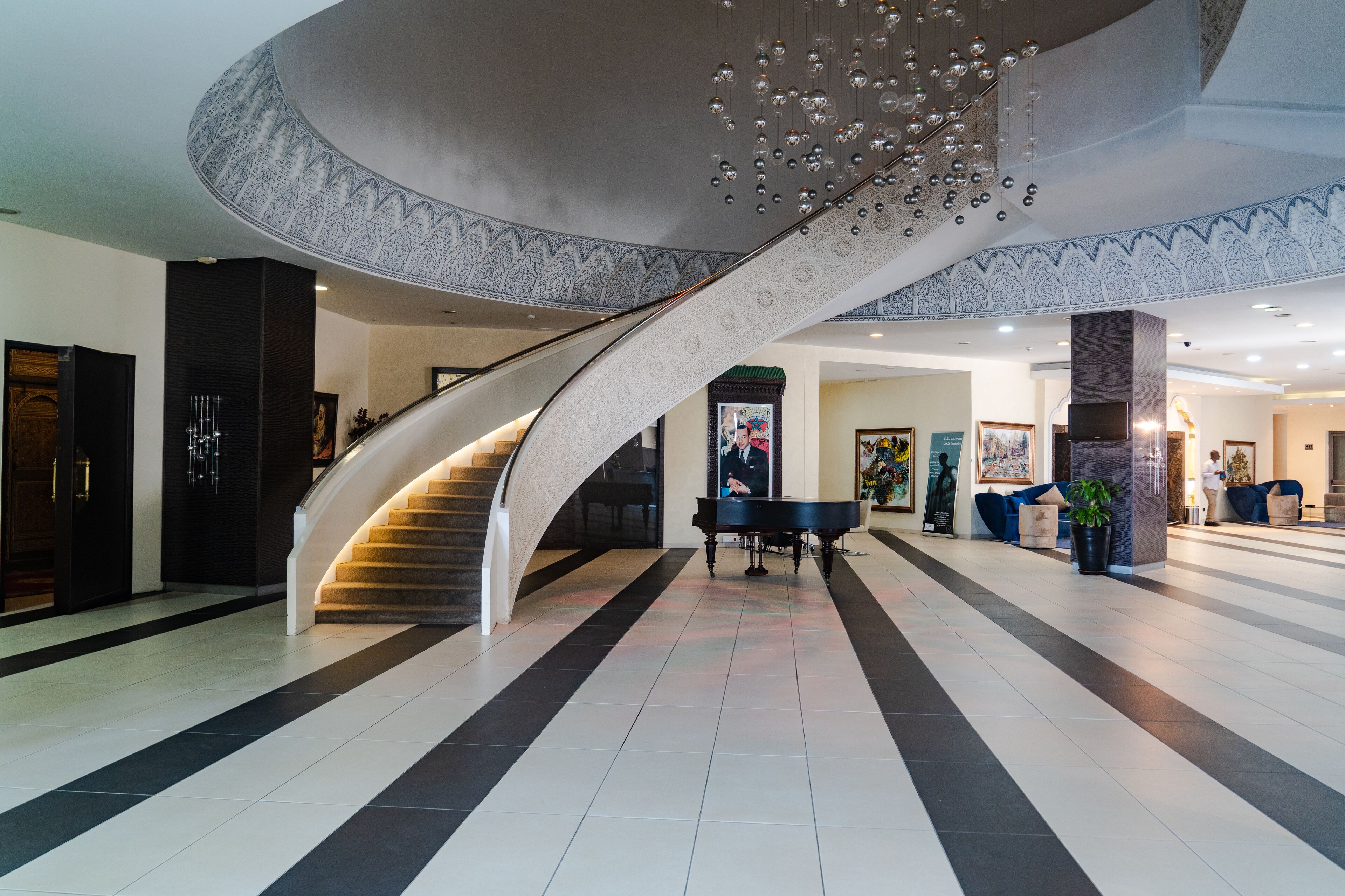 A grand lobby with a curved staircase, a grand piano, and a reception area.