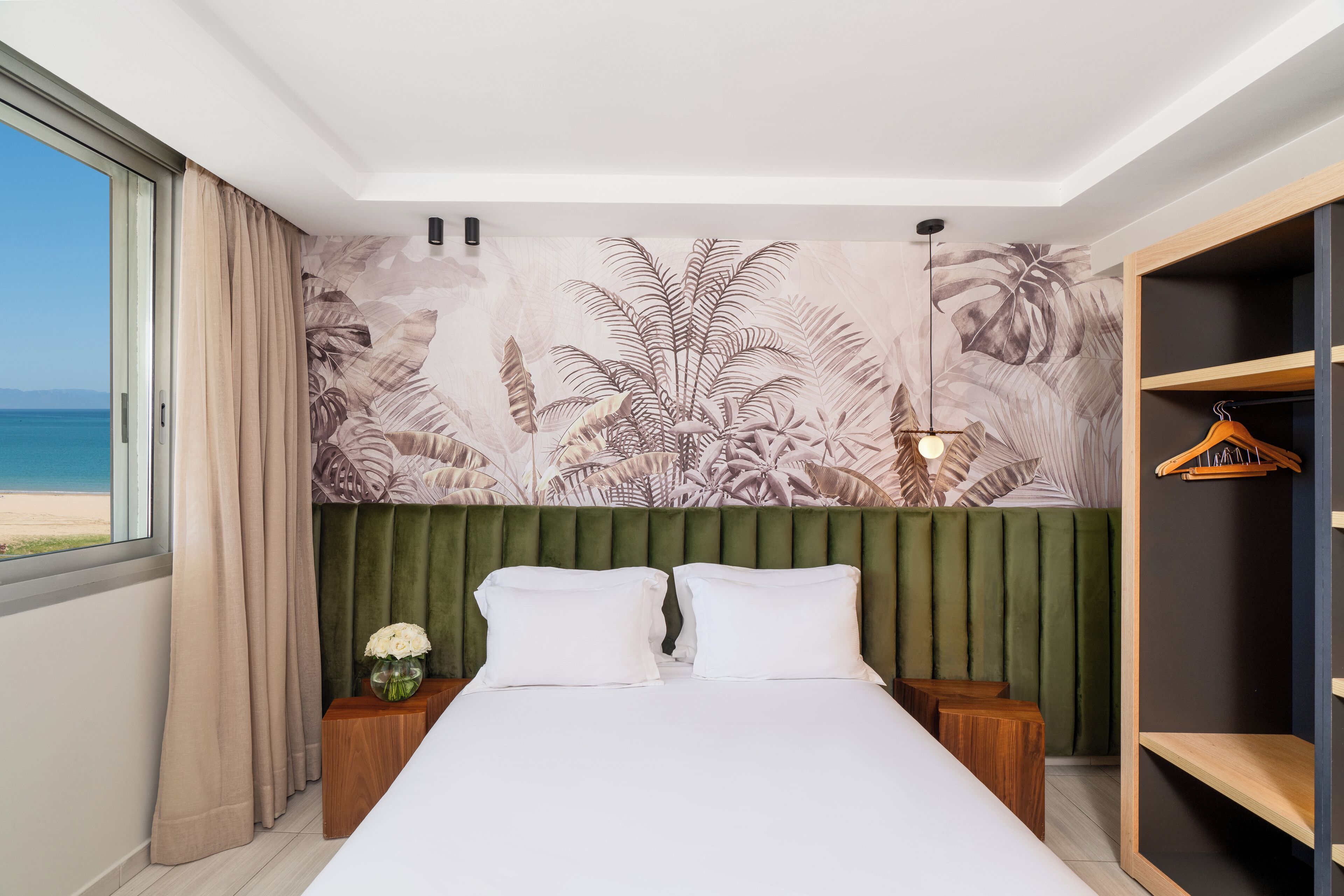 Une chambre d’hôtel avec un lit, une table de chevet, un porte-manteau et une vue sur la plage.
