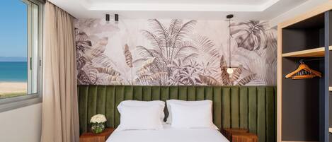 Une chambre d’hôtel avec un lit, une table de chevet, un porte-manteau et une vue sur la plage.