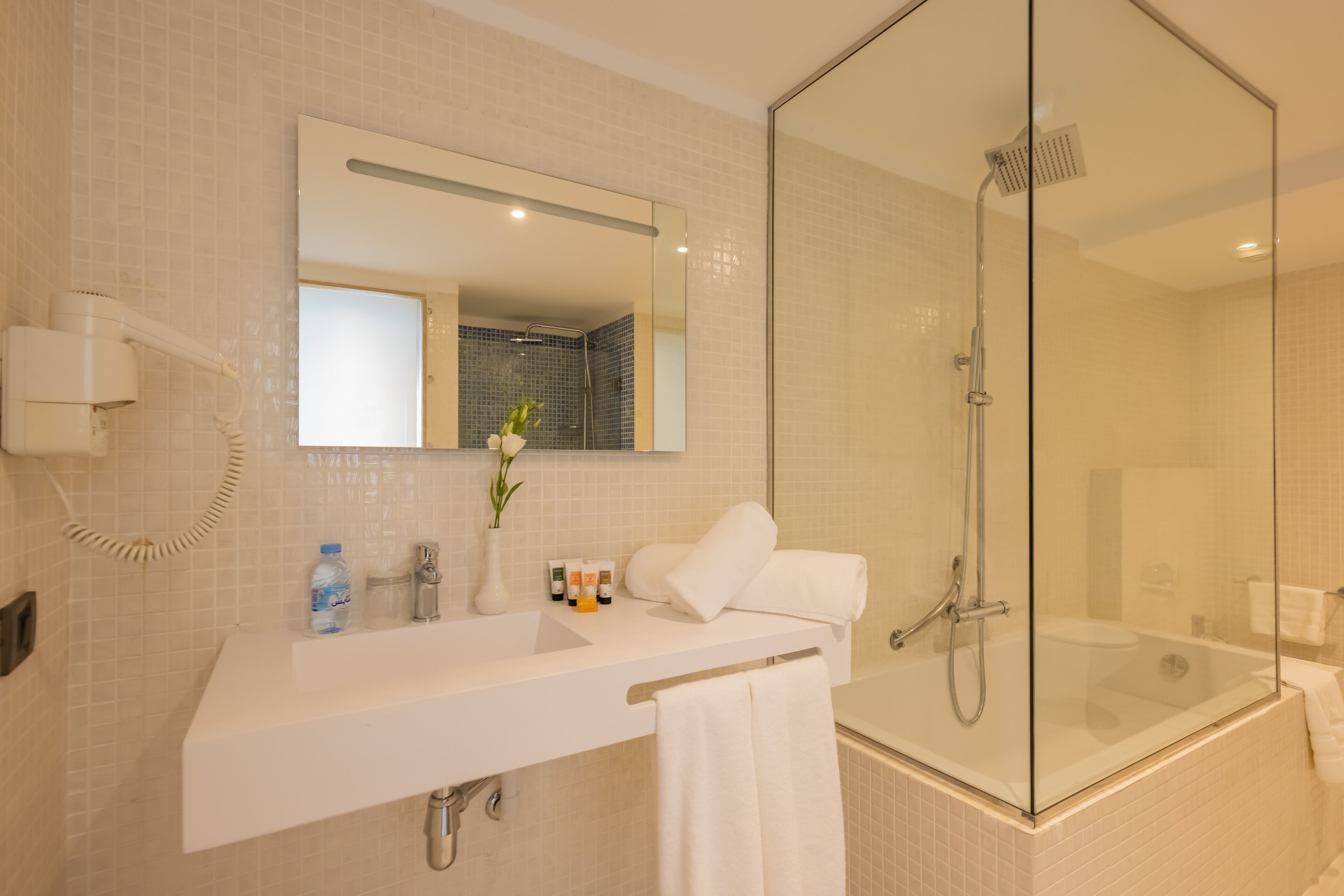 Un baño moderno con ducha acristalada, un lavabo blanco, un espejo y un secador de pelo.