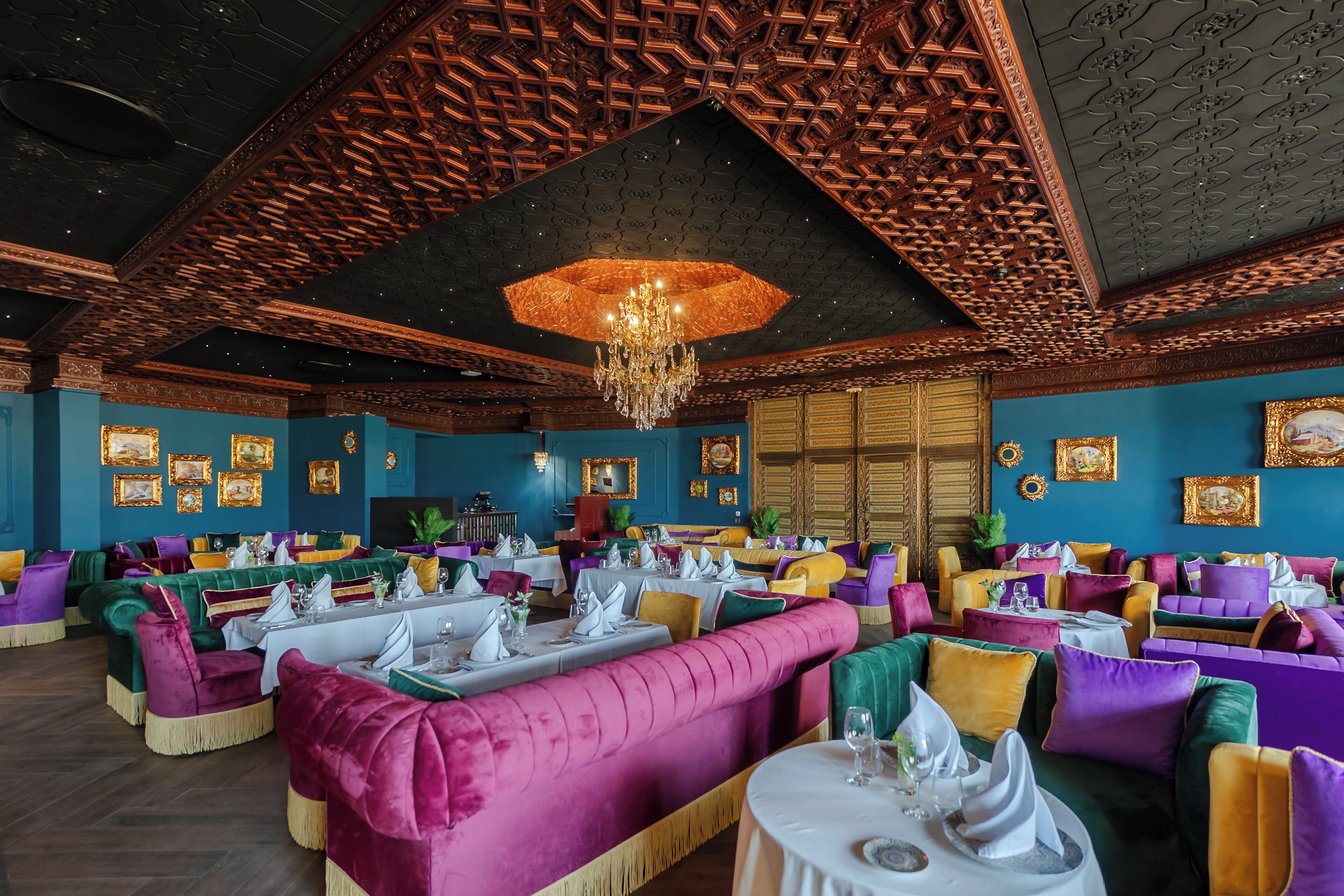A restaurant with vibrant seating areas, a chandelier, and framed artwork on the walls.