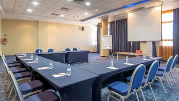 Un salón de conferencias con una larga mesa, sillas, una pantalla de proyector y una pizarra.