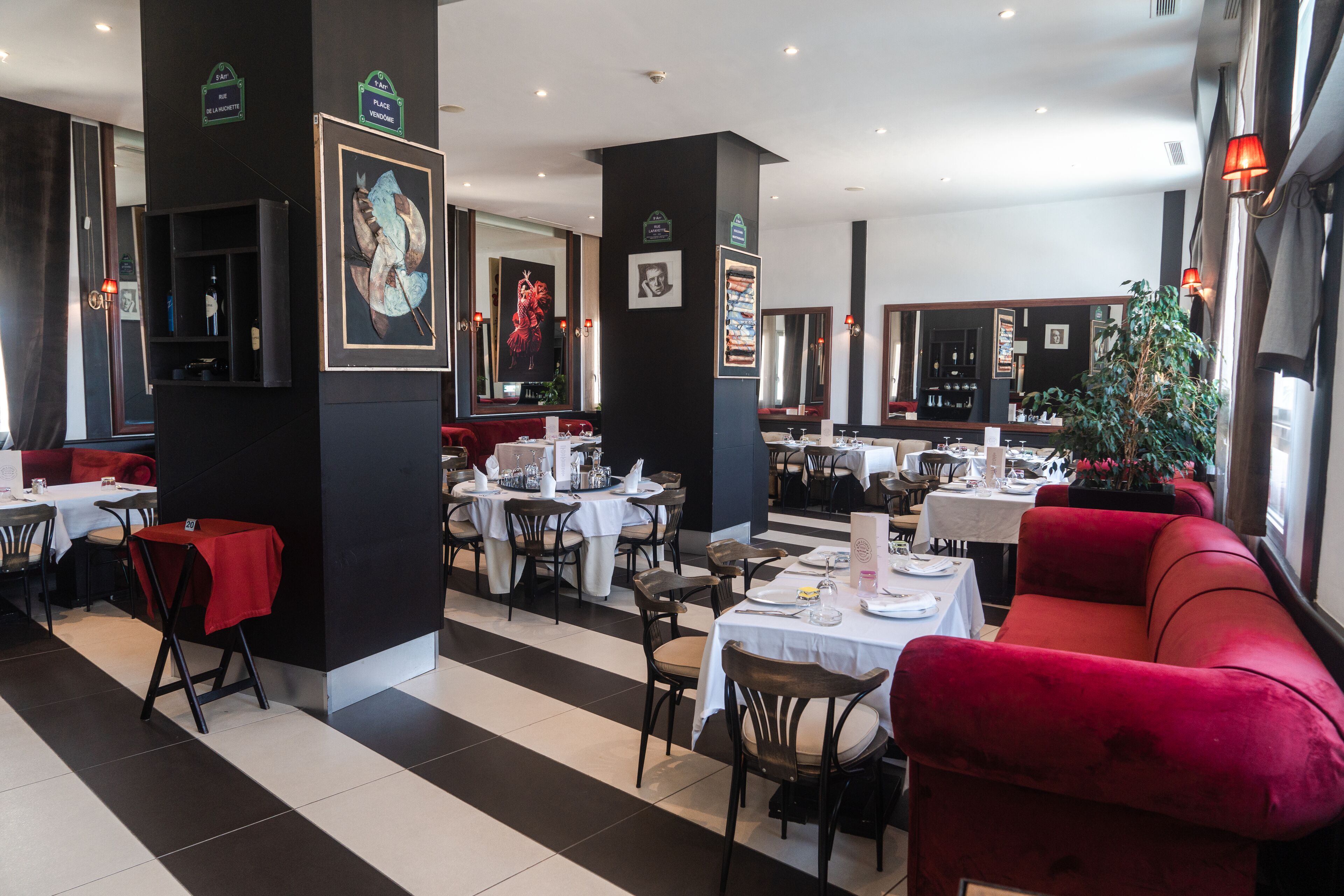 Un restaurant dont le sol est recouvert de carreaux noirs et blancs, qui propose des sièges rembourrés de couleur rouge et dont les murs sont ornés d’œuvres d’art encadrées.