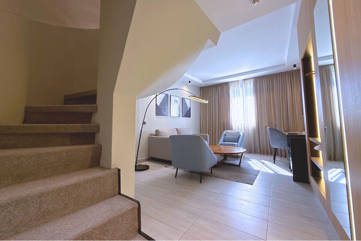 A spacious living area with a staircase, a sofa, a chair, and a coffee table.