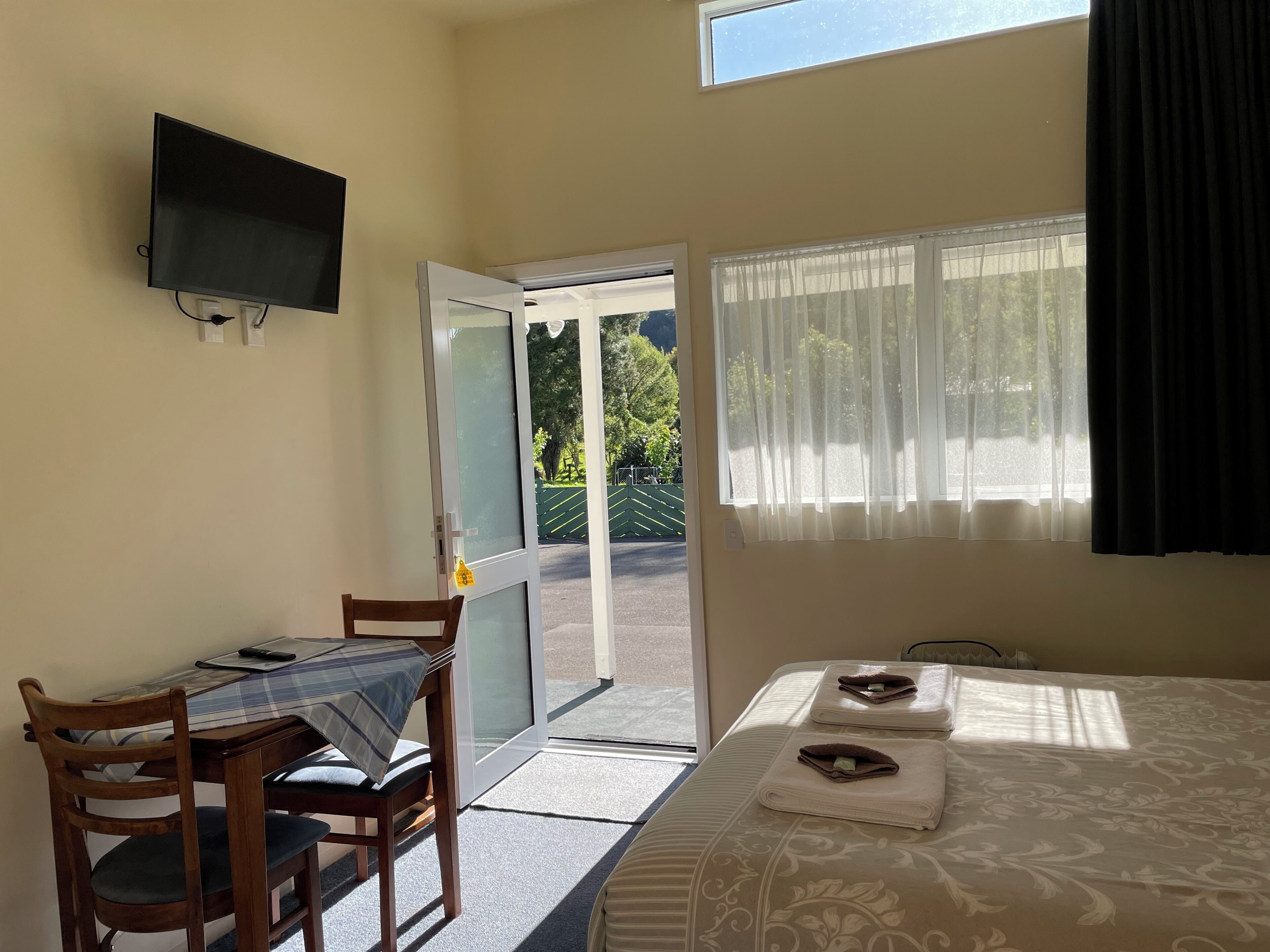 Ein Zimmer mit einem Bett, einem Tisch mit Stühlen, einem Fernseher und einer zur Außenwelt führenden Tür.