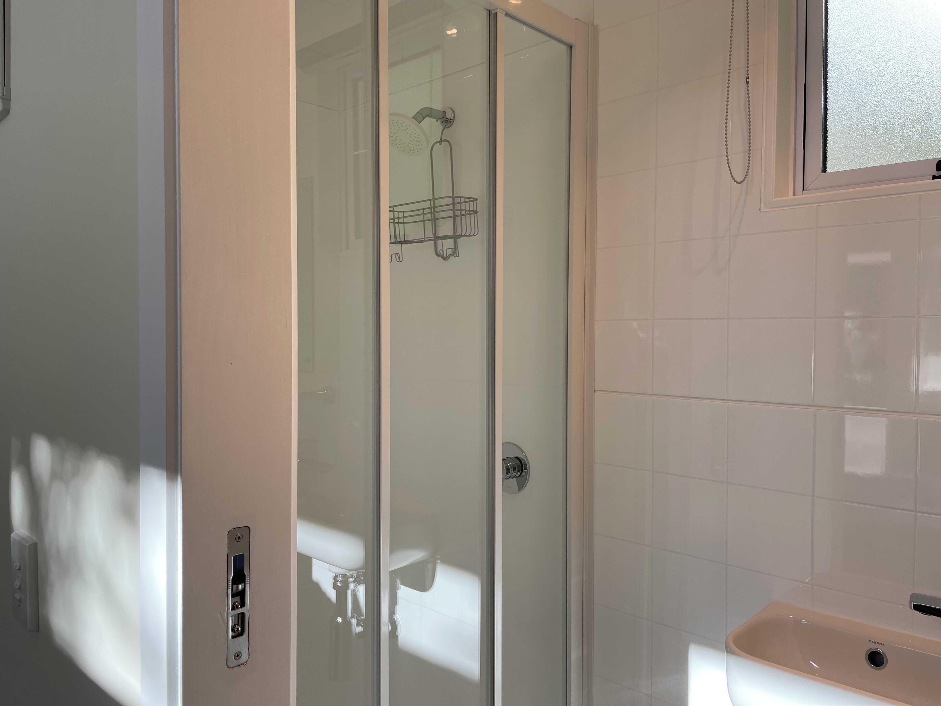 A modern bathroom with a glass-enclosed shower, a white sink, and a window.