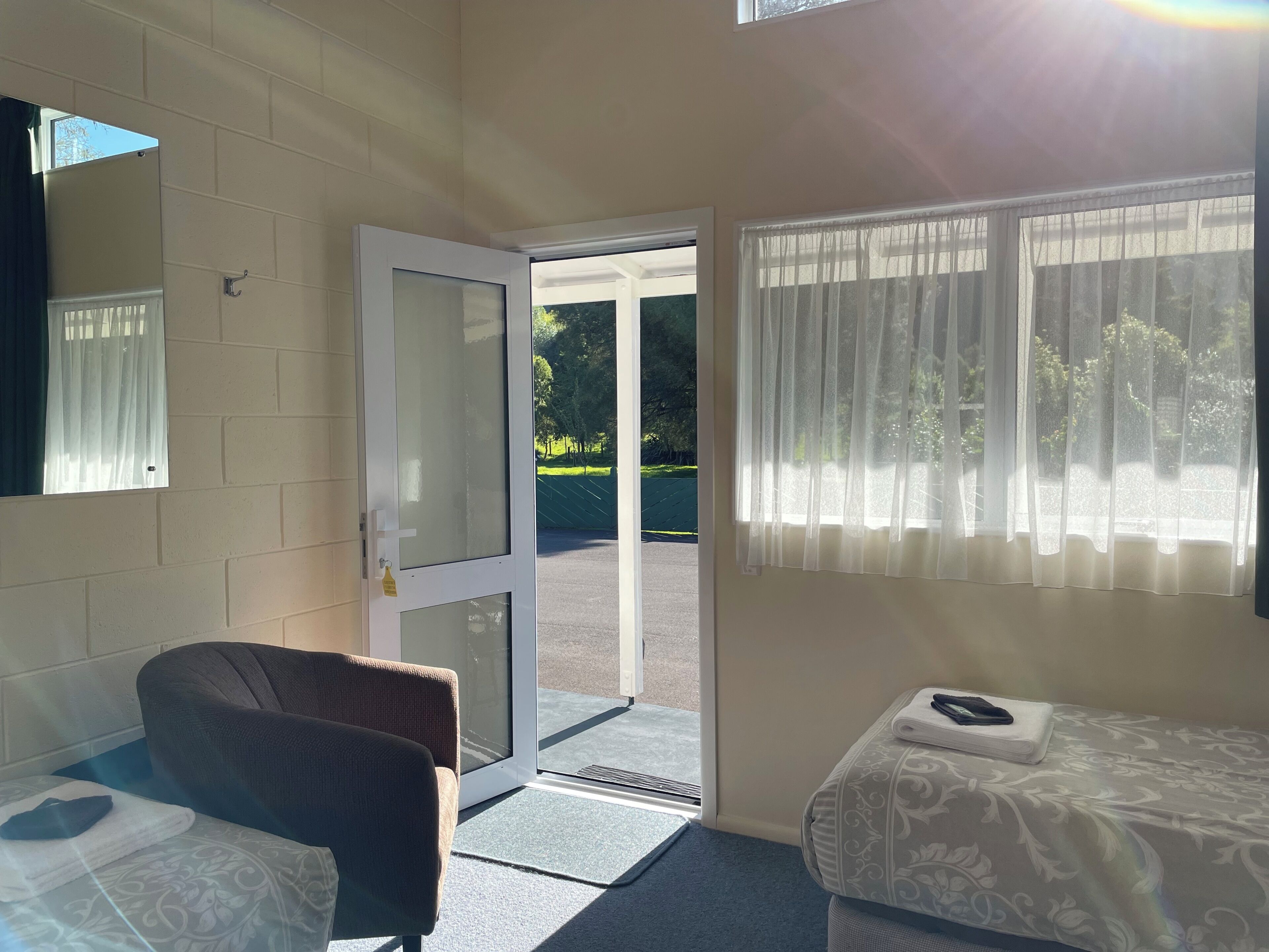 A room with a bed, a chair, a door leading outside, and a window with curtains.