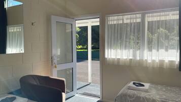 A room with a bed, a chair, a door leading outside, and a window with curtains.