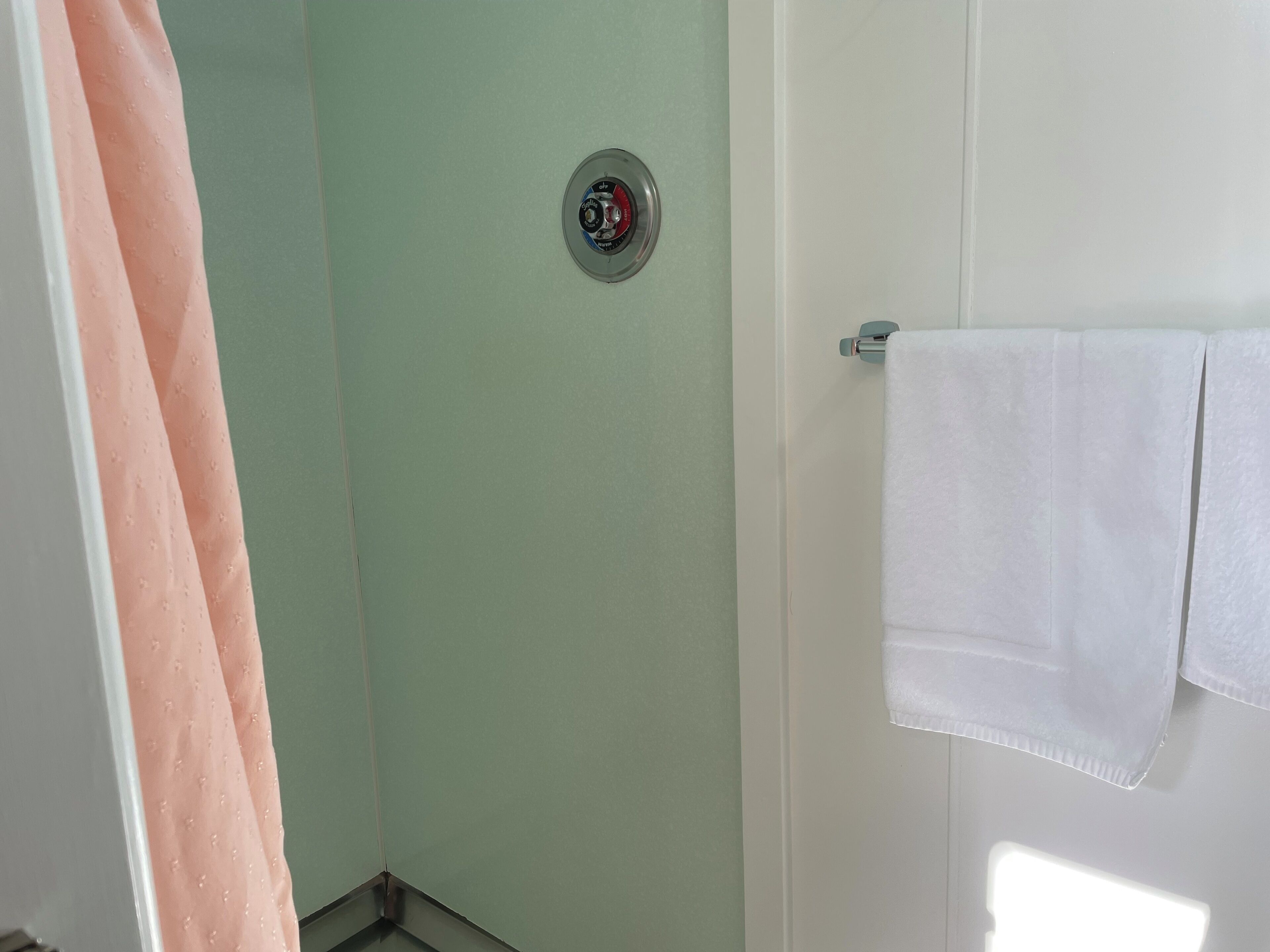 A bathroom with a shower curtain, a towel rack with a white towel, and a wall-mounted flush toilet.