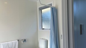 A bathroom with a toilet, a towel rack with a white towel, a window with a blue curtain, and a door.