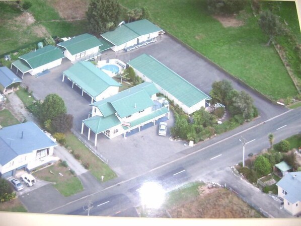A multi-story building with a green roof, several parking spaces, and a swimming pool.