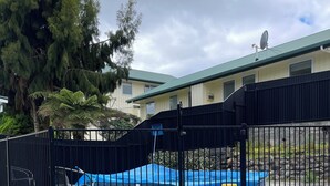 A gated area with a blue pool, a satellite dish on a building, and a large tree.