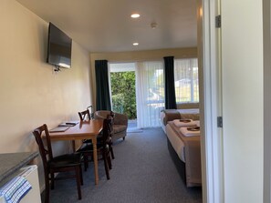 A compact room with a dining table, chairs, a sofa, and a bed. A flat-screen TV is mounted on the wall. - Mataki Motels (Murchison)