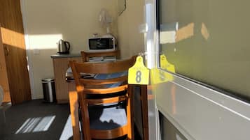 A compact kitchen with a microwave, a small trash bin, and a wooden chair with a cushion.