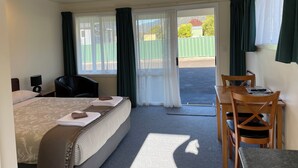A hotel room with a bed, a desk with a chair, and a view of a fenced outdoor area.