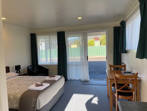 A hotel room with a bed, a desk with a chair, and a view of a fenced outdoor area.