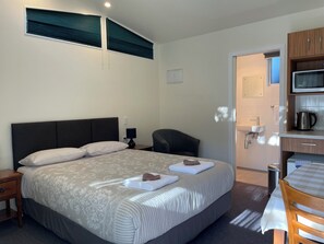 Habitación de hotel con una cama grande, una mesita de noche, una silla, un escritorio con silla, un microondas y un lavamanos.