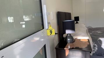 Habitación de hotel con una cama, una mesita de noche con lámpara, una ventana con vidrio esmerilado y un cartel que indica el número de habitación 9.