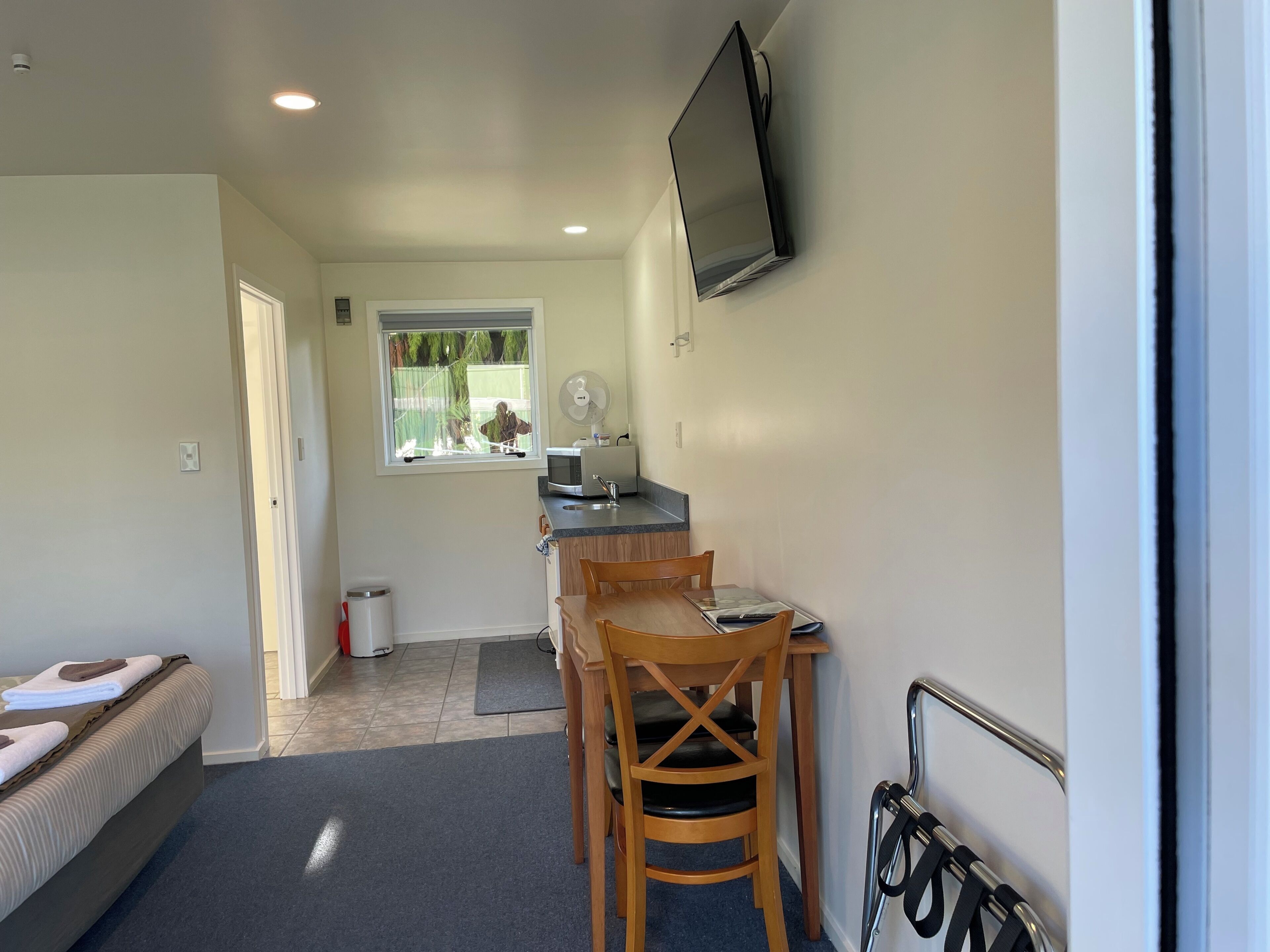 A compact room with a kitchenette, a dining area, and a TV mounted on the wall.