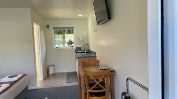 A compact room with a kitchenette, a dining area, and a TV mounted on the wall.