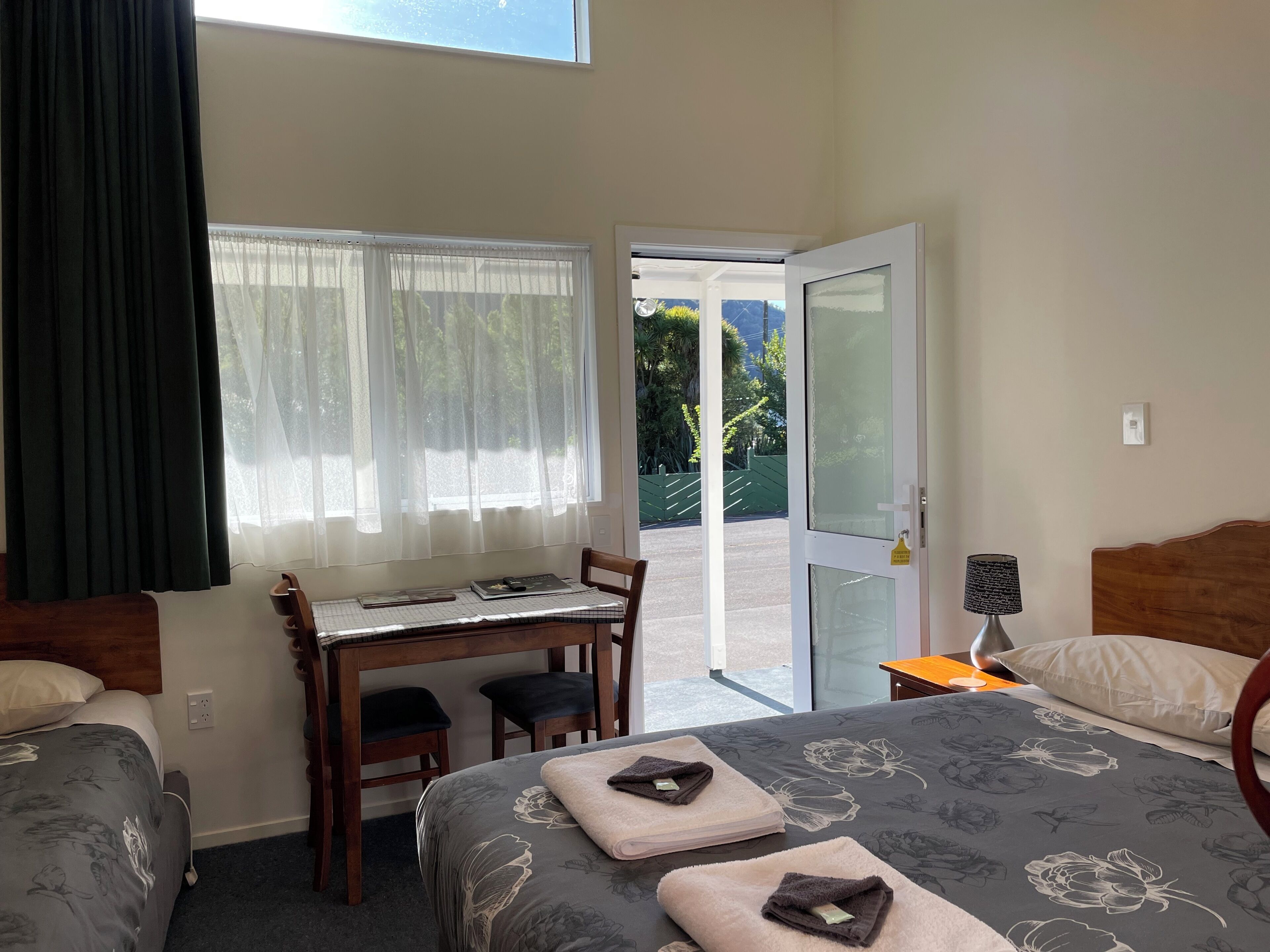 A hotel room with a bed, a desk, and a chair. There is a door leading to an outdoor area.