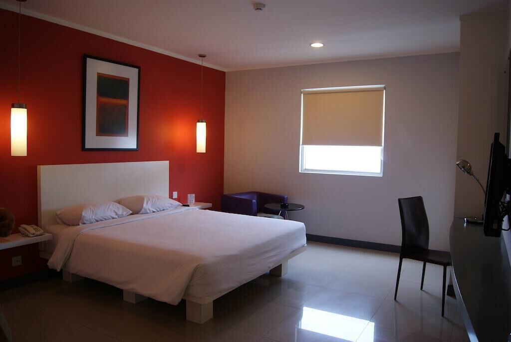 Ein Hotelzimmer mit Bett, Schreibtisch, Stuhl, Fenster und einem Bild an der Wand.