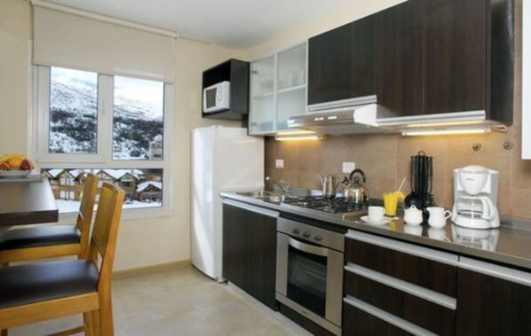 A modern kitchen with dark cabinets, a stove, and a microwave. There is a window with a view of a snowy landscape.