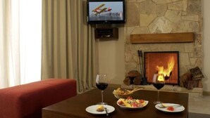 A dining area with a stone fireplace, a television mounted on the wall, and two glasses of red wine on the table. - Village Condo (San Carlos de Bariloche)