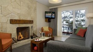 A living room with a stone fireplace, a television mounted on the wall, a sofa, and a balcony with a view of trees. - Village Condo (San Carlos de Bariloche)