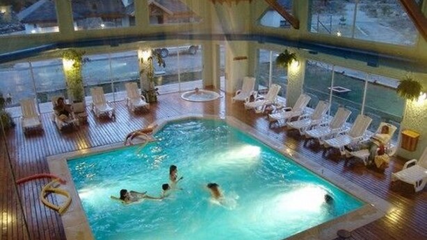An indoor swimming pool with multiple lanes, surrounded by lounge chairs and a wooden deck. - Village Condo (San Carlos de Bariloche)