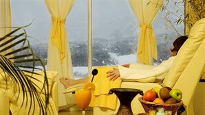 A room with a large window, a table with a fruit basket, a glass of orange juice, and a coffee maker. - Village Condo (San Carlos de Bariloche)