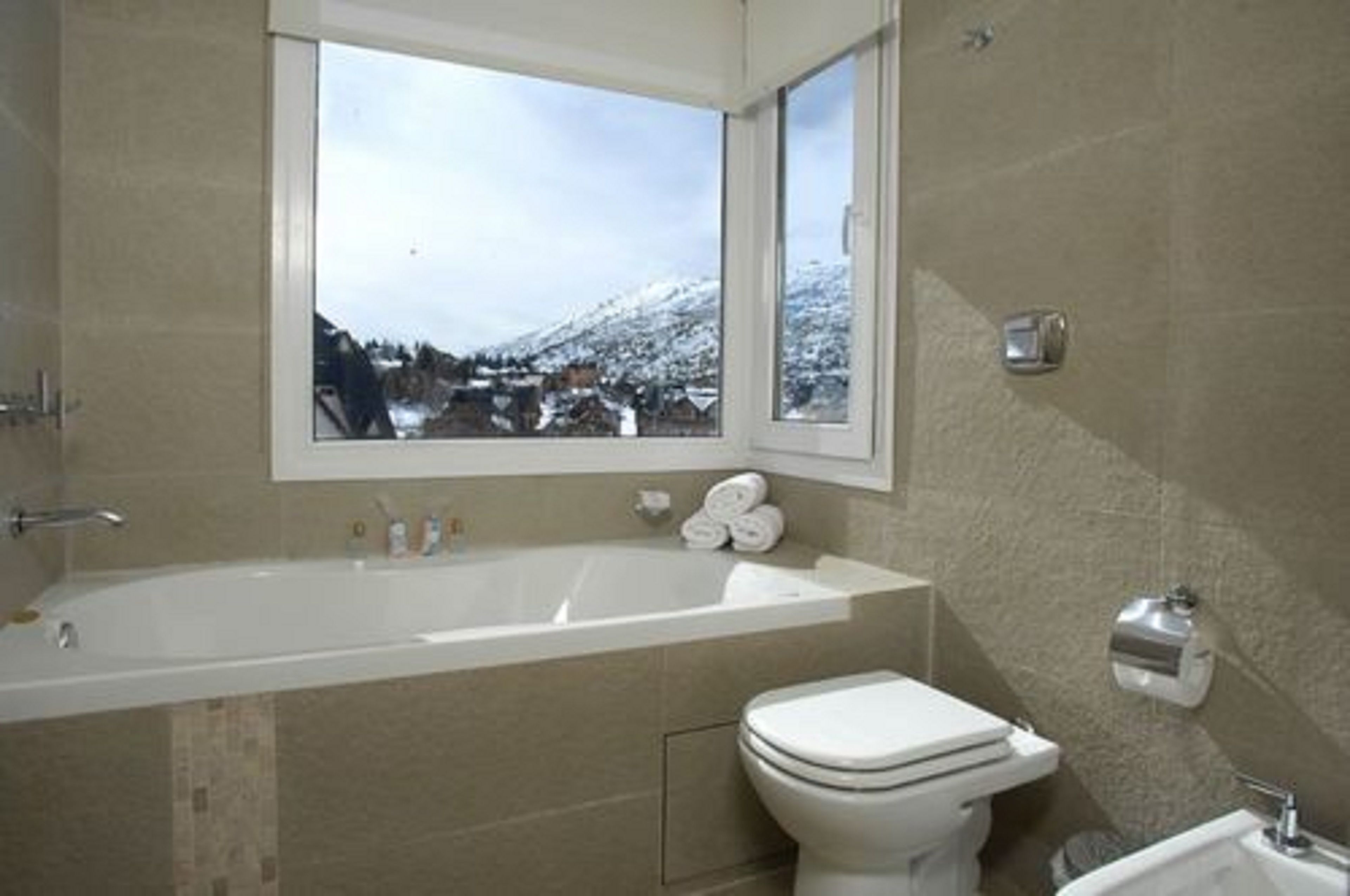 Un ba ño con bañera, inodoro y ventana con vista a un pueblo nevado.