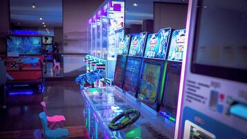 Uma fileira de máquinas de jogos eletrônicos com luzes de néon, uma vitrine de vidro e algumas cadeiras em um ambiente com pouca luz.