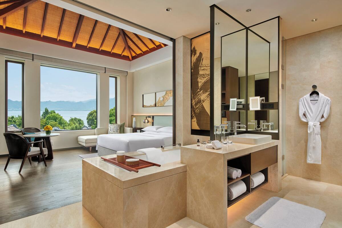 Une chambre d’hôtel moderne dotée d’une grande fenêtre, d’une salle de bain privée, d’un coin repas et offrant une vue sur les montagnes.