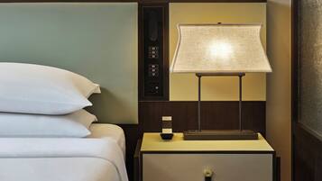 A hotel room with a bed, a nightstand with a lamp, and a wall-mounted artwork.