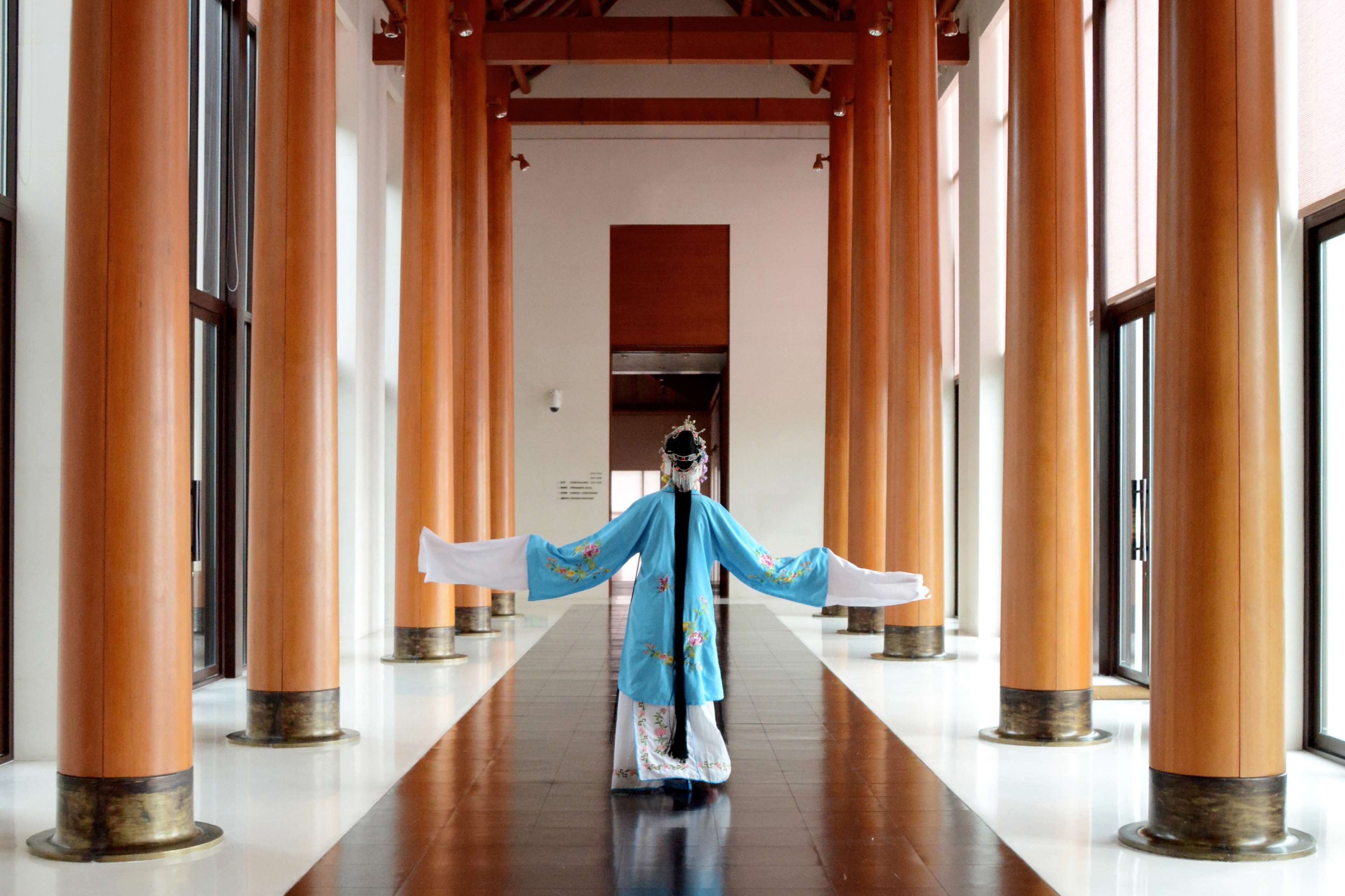 Un pasillo con columnas de madera y una persona vestida con traje tradicional.