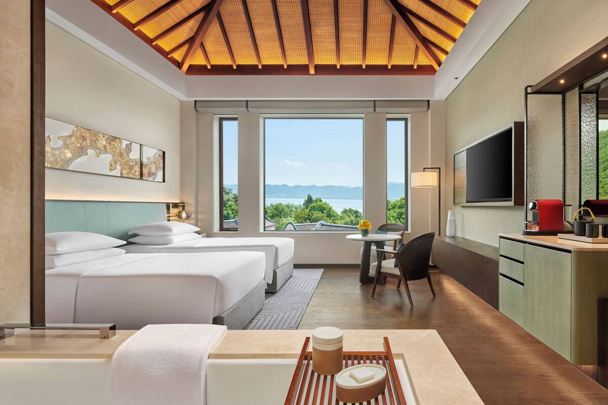 Une chambre d’hôtel avec deux lits, un coin repas, une cuisine et une grande fenêtre donnant sur l’extérieur.