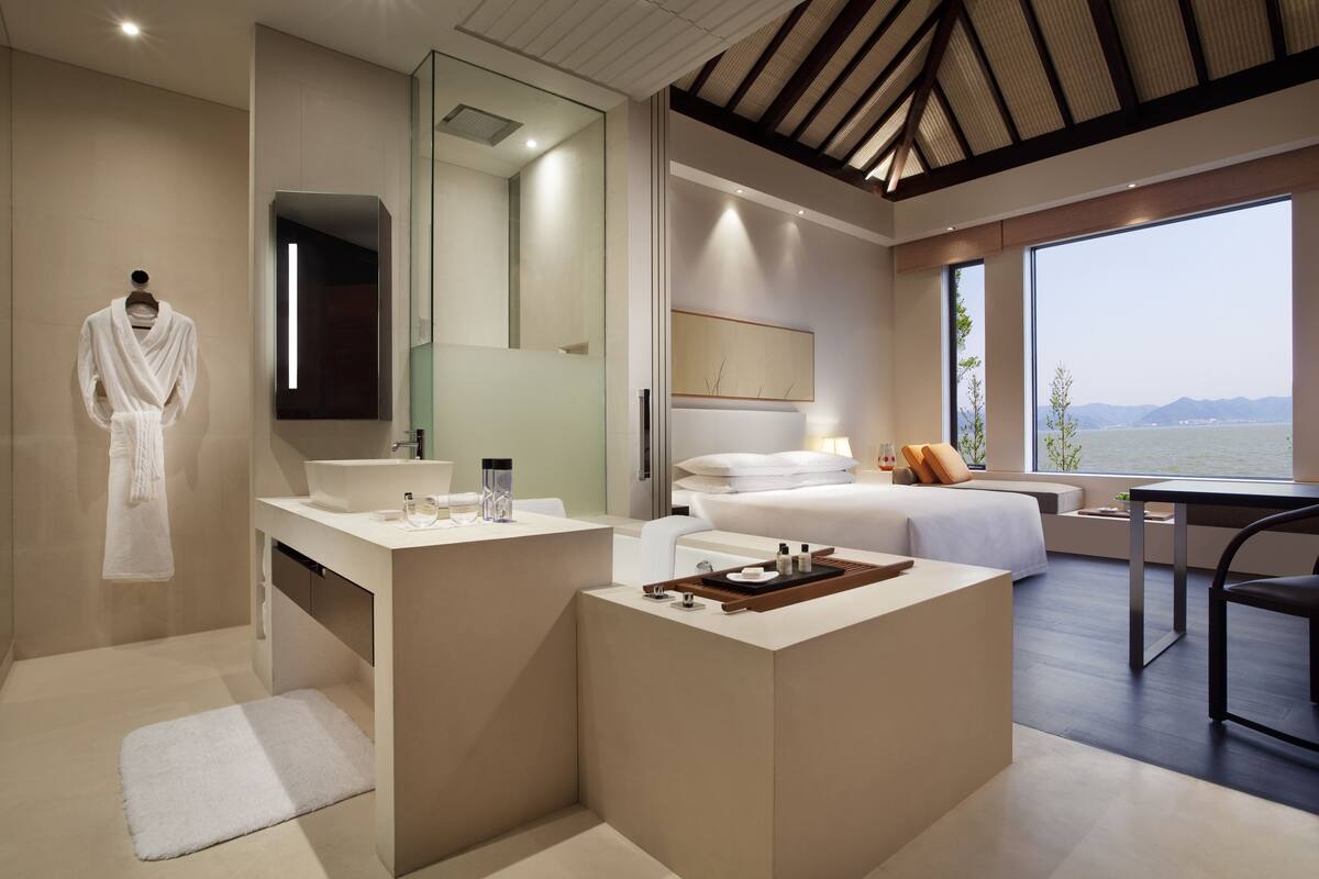 Une chambre d’hôtel moderne dotée d’un grand lit, d’un coin salon avec vue, d’une coiffeuse avec miroir et d’un peignoir accroché au mur.