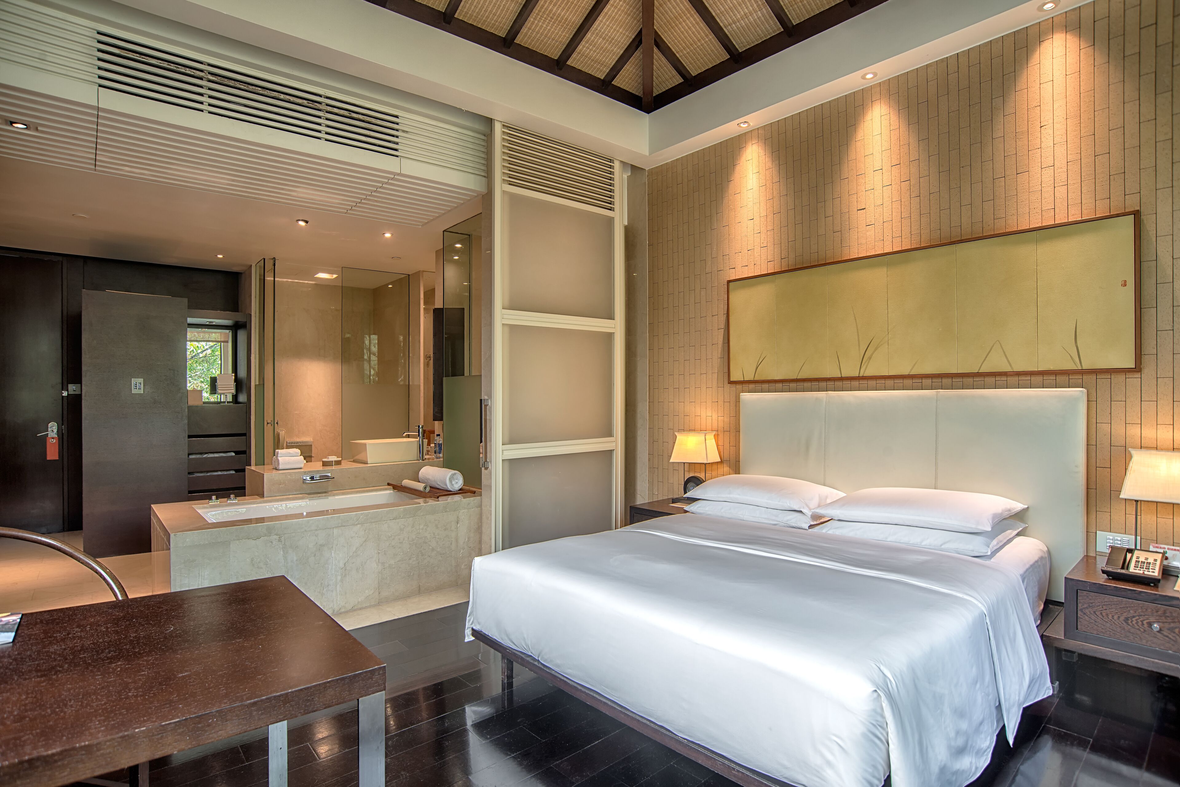 Een moderne hotelkamer met een groot bed, een aparte badkamer, een bureau en een groot kunstwerk aan de muur.