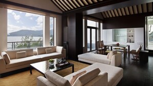 Amplia sala de estar con un sofá grande, una mesa de centro y una mesa de comedor. Grandes ventanales ofrecen vistas al exterior.