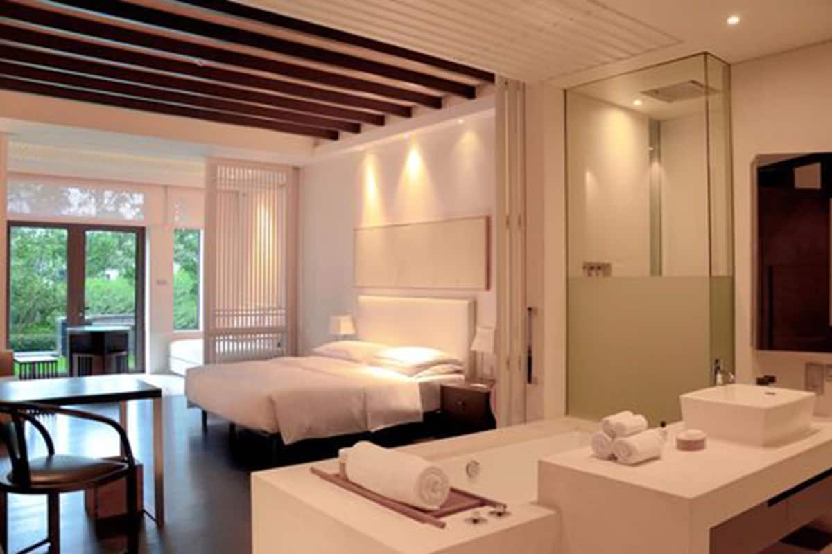 Une chambre d’hôtel moderne équipée d’un lit, d’un bureau, d’un grand miroir et d’une salle de bain avec un lavabo et un miroir.